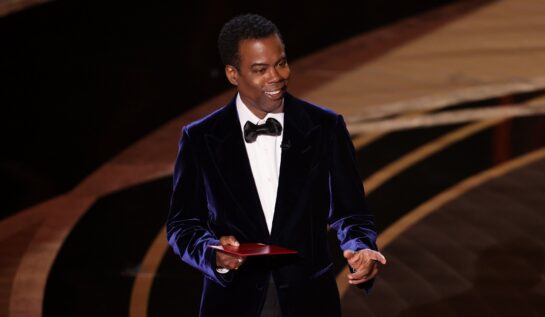 Chris Rock îmbrăcat la costum în timp ce prezintă pe scena premiilor Oscar 2022