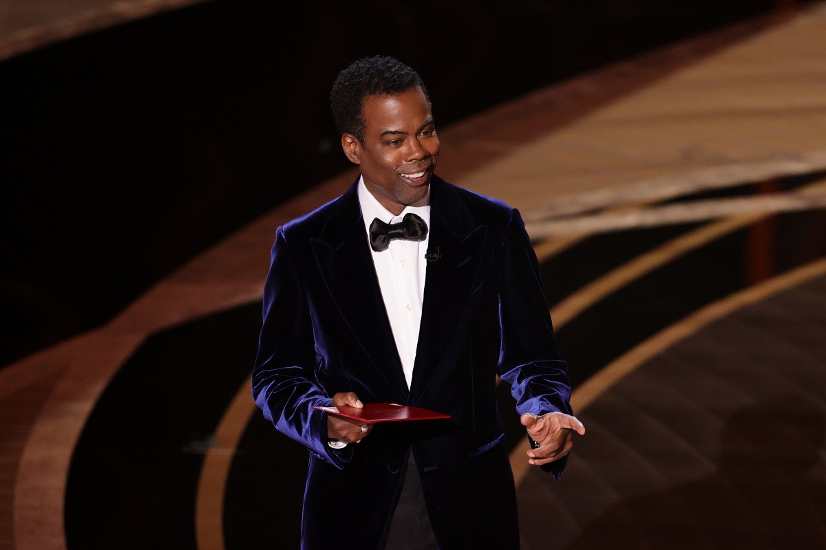 Chris Rock îmbrăcat la costum în timp ce prezintă pe scena premiilor Oscar 2022