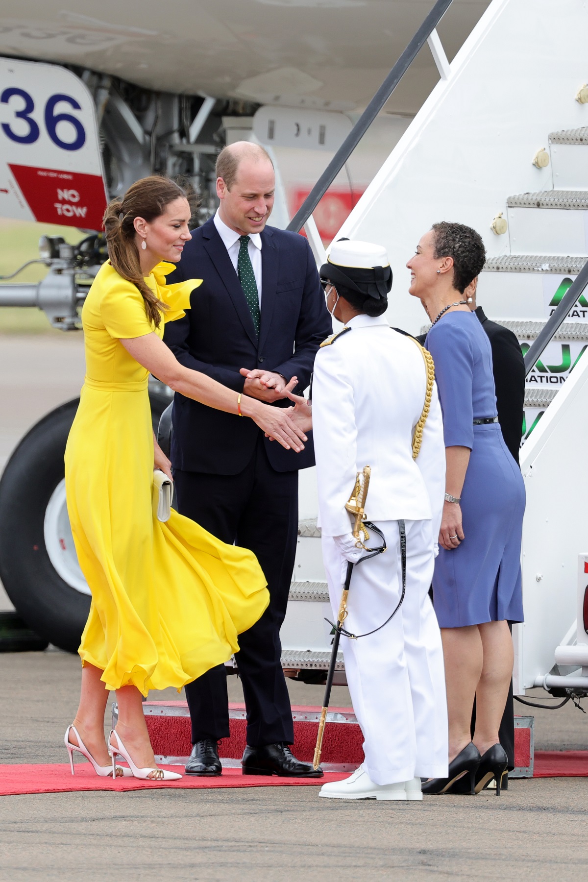 Kate Middleton într-o rochie galbenă alături de Prințul William îmbrăcat la costum în timpc e vcoboraă din avion pentru ase întâlni cu oficialii din Jamaica