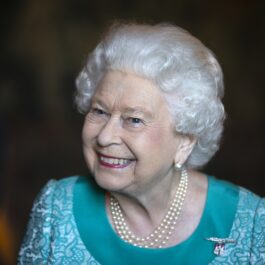Regina Elisabeta îmbrăcată într-un costum albastru în timp ce zâmbește la o întâlnire publică