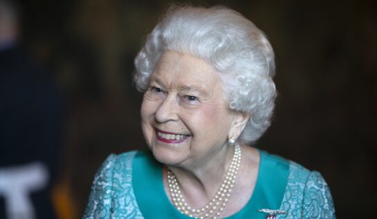Regina Elisabeta îmbrăcată într-un costum albastru în timp ce zâmbește la o întâlnire publică