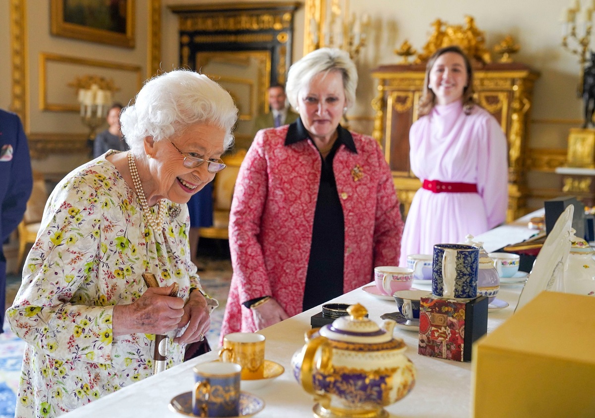 Regina Elisabeta într-o rochie cu imprimeu floral în timp ce privește obectele de porțelan de la expoziția ținută la Castelul Windsor