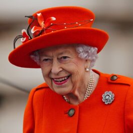 Regina Elisabeta îmbrăcată într-un costum portocaliu cu pălărie la un eveniment special de la Palatul Buckingham din anul 2021
