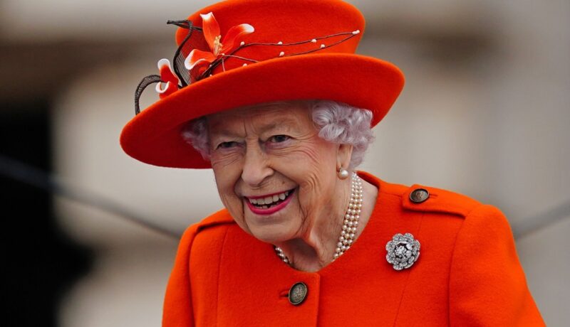 Regina Elisabeta îmbrăcată într-un costum portocaliu cu pălărie la un eveniment special de la Palatul Buckingham din anul 2021