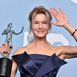 Renée Zellweger într-o rochie gri în timp ce ține în mână o statuetă