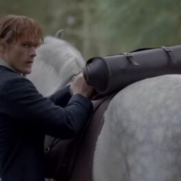 Actorul Sam Heughan în rolul lui Jamie Fraser în timp ce mângâie un cal alb