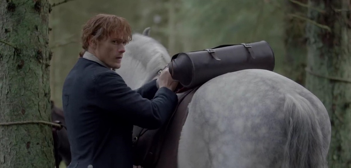 Actorul Sam Heughan în rolul lui Jamie Fraser în timp ce mângâie un cal alb