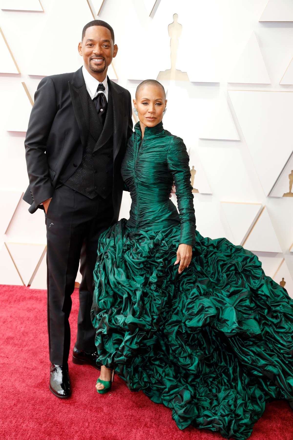Jada și Will Smith îmbrăcați elegant, Jada cu o rochie verde și Will la costum, în timp ce pozează pe covorul roșu de la Gala Premiilor Oscar 202