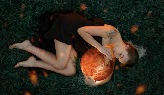 Femeie frumoasă stă întinsă pe jos și ține un glob portocaliu în mână