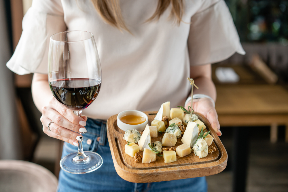 O femeie care ține în mână un platou cu brânzeturi și un pahar cu vin