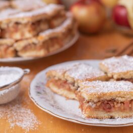 Plăcintă cu mere de post, porționată pe două farfurii și decorată cu zahăr pudră