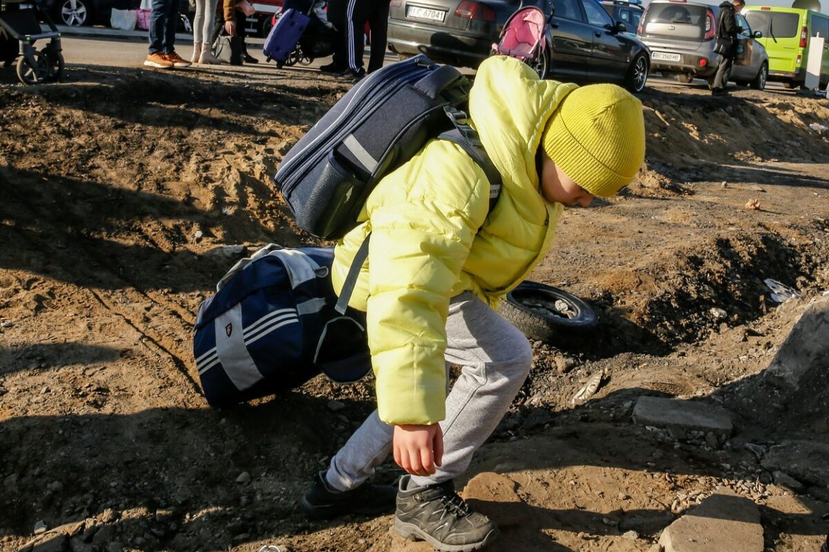 Un băiețel în geacă verde, care trage de niște bagaje și trece granița în Ucraina
