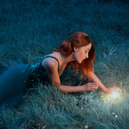 Fată frumoasă stă întinsă pe iarbă și se uită la o sursă de lumină