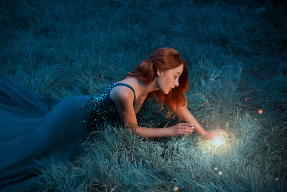Fată frumoasă stă întinsă pe iarbă și se uită la o sursă de lumină