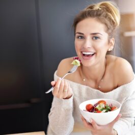 O femeie frumoasă care mănâncă dintr-un bol alb de salată cu dressing pentru a demonstra unul din principalelle obiceiuri alimentare care duc la acumularea rapidă a grăsimii abdominale
