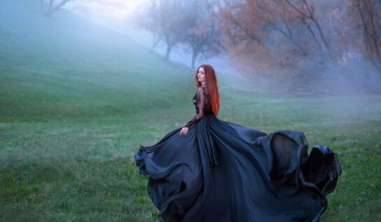 Fată frumoasă cu rochie lungă și păr roșu se plimbă prin pădure