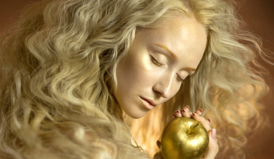 Fată frumoasă cu părul de aur, ține ochii închiși și un măr auriu în mână