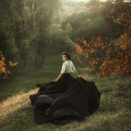 Fată frumoasă cu rochie lungă, neagră se plimbă prin pădure
