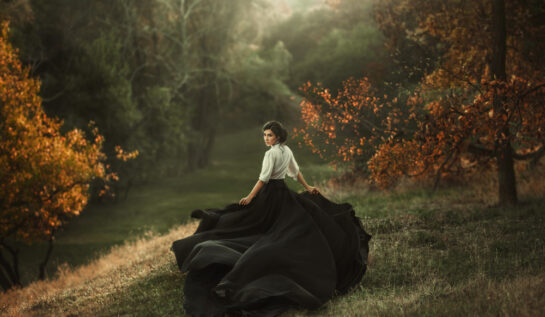 Fată frumoasă cu rochie lungă, neagră se plimbă prin pădure