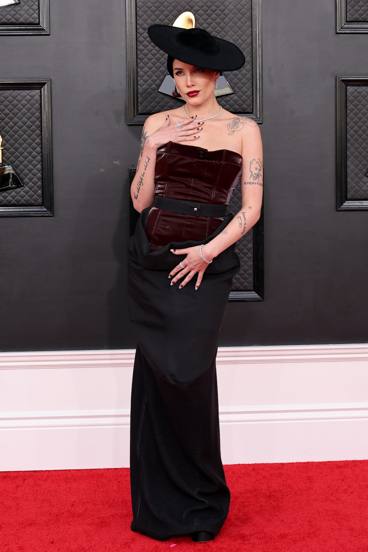 Cântăreața Halsey într-o rochie neagră cu o pălărie în timp ce pozează pe covorul roșu de la Premiile Grammy 2022