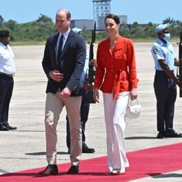 Kate Middleton într-un sacou portocaliu și o pereche de pantaloni albi alături de Prințul William în timp ce se întâlnesc cu un reprezentant oficial din Jamaica