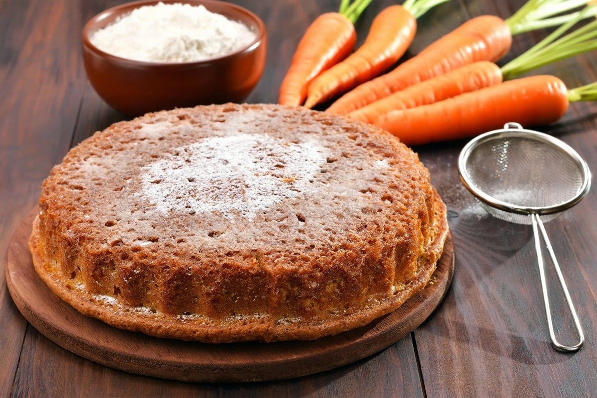 Prăjitură cu morcovi decorată cu zahăr, alături de morcovi și o sită