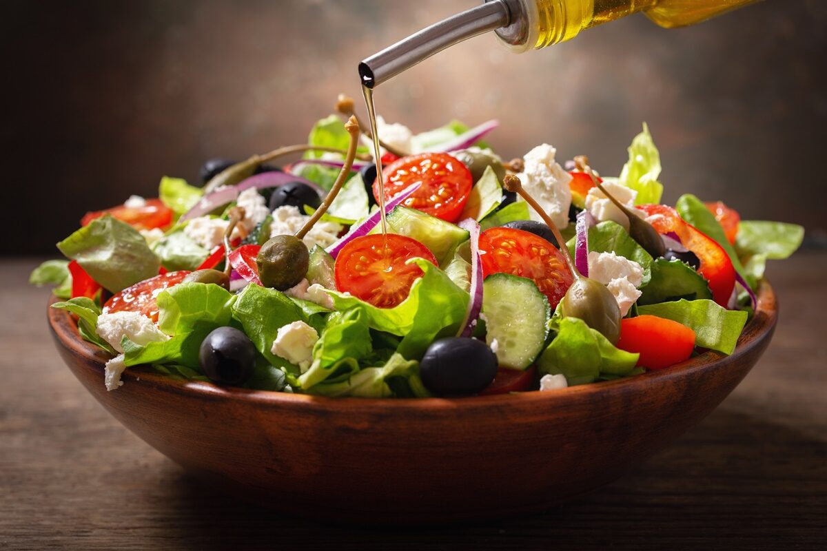 Bol cu salată grecească și recipient cu ulei de măsline