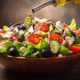 Bol cu salată grecească și recipient cu ulei de măsline