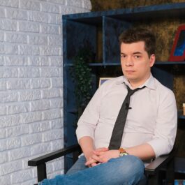 invitatul de la interviul CaTine.ro la masculin, Toma Alexandru, în timp ce oartă o cămașă albă și o cravată neagră și pozează pe platourile de filmare