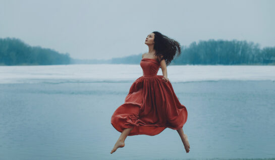 Fată frumoasă brunetă îmbrăcată cu o rochie roșie lungă se află pe gheață