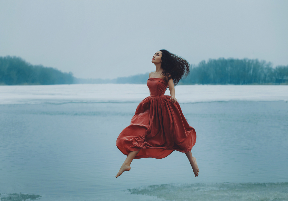 Fată frumoasă brunetă îmbrăcată cu o rochie roșie lungă se află pe gheață