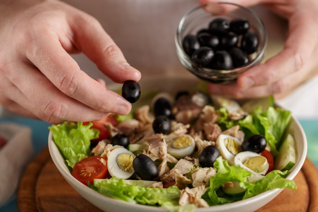 The step of adding olives to a bowl of lettuce, tomatoes, cucumbers and tuna