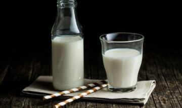 Un blat de lemn pe care se află o sticlă și un pahar pline cu lapte pentru a ilustra ce se poate întâmpla dacă renunți la consumul de lapte de vacă