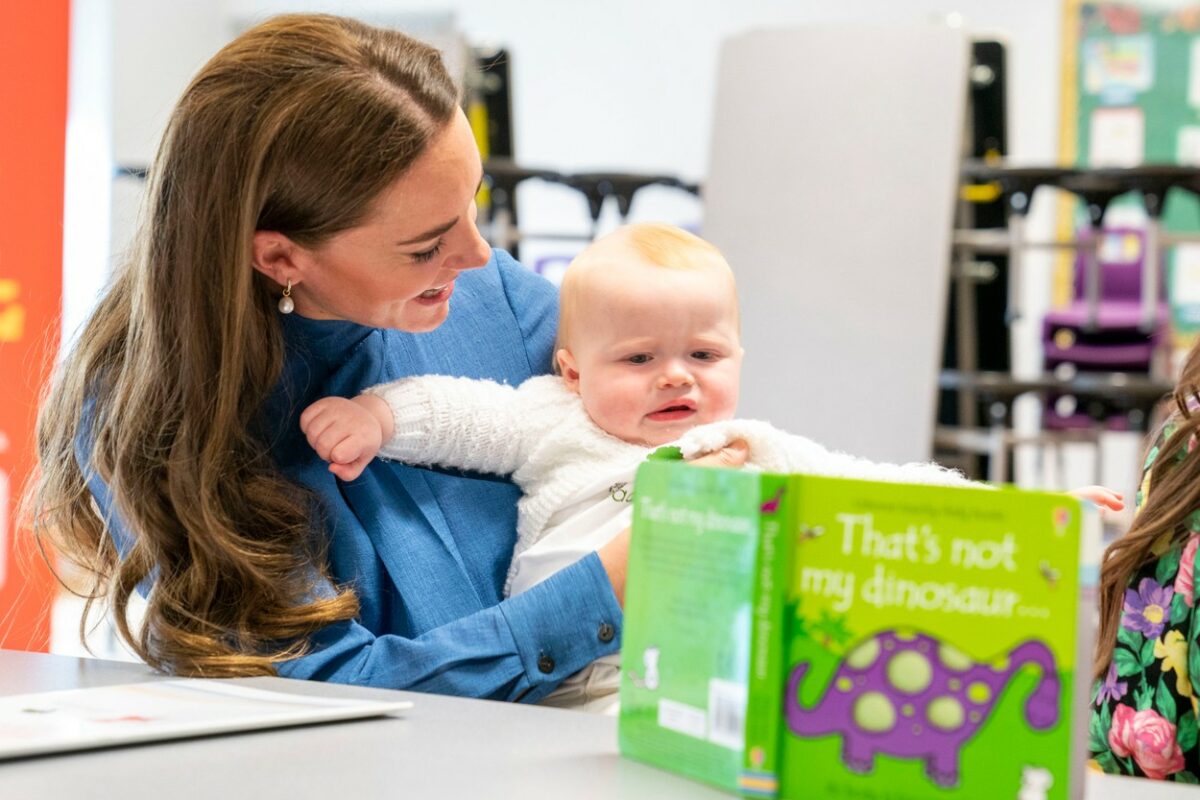 Kate Middleton, ține în brațe un bebeluș și se uită împreună pe o carte
