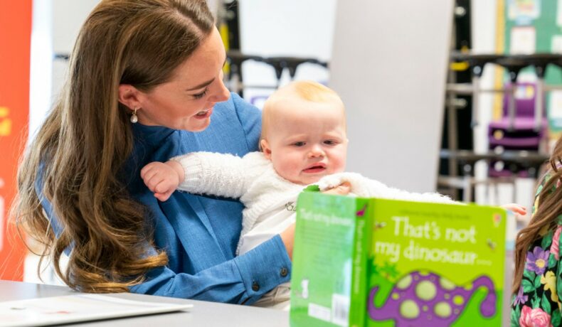 Kate Middleton, ține în brațe un bebeluș și se uită împreună pe o carte