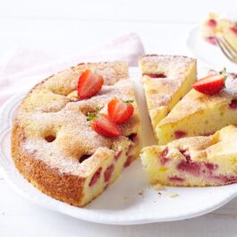 Prăjitură pufoasă cu căpșuni porționată pe un platou rotund și pe o farfurie
