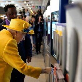 Regina Elisabeta într-un costum galben în timp ce cumpără o cartelă de metrou de la Paddington Station pentru a călătorii cu pe linia de metrou care îi poartă numele, Elizabeth Line