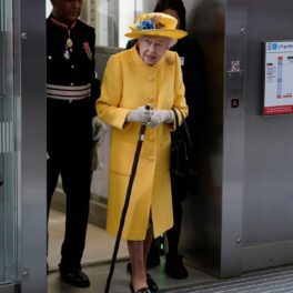 Regina Elisabeta în timp ce poartă un costum galben și coboară dintr-un lift pentru a participa la inaugurarea Elizabeth line de la Paddington Station