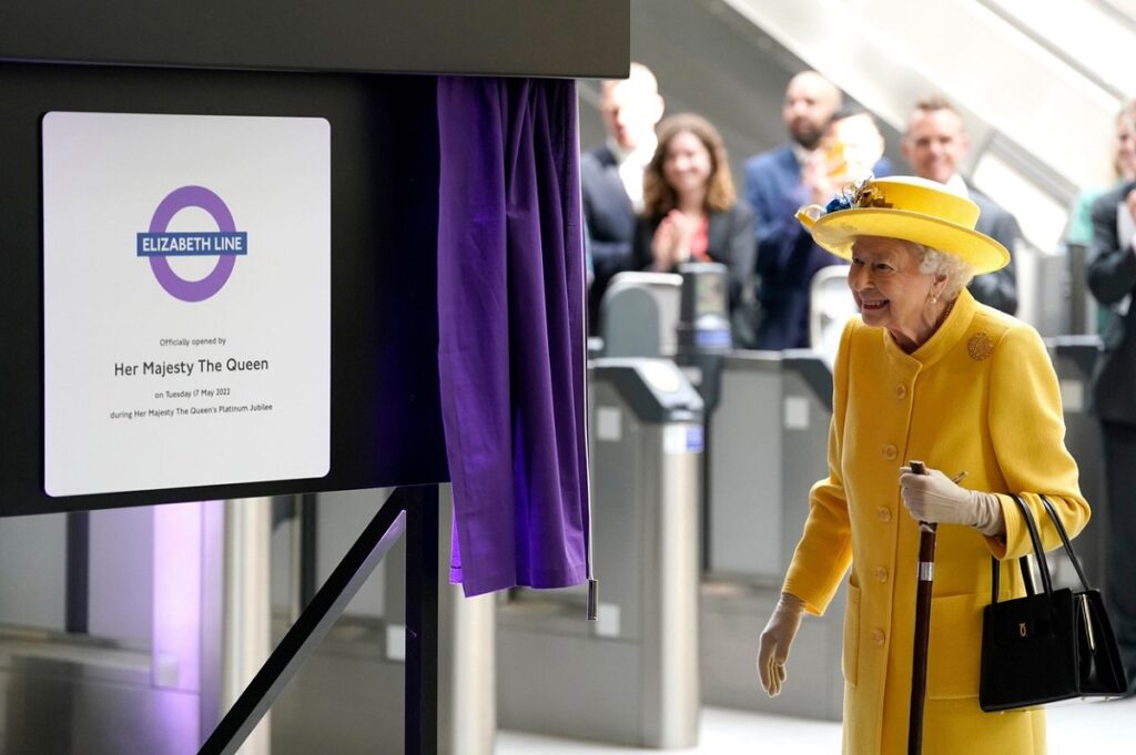 Regina Elisabeta îmbrăcată într-un costum galben în timp ce ia parte la inaugurarea Elizabeth line de la Paddington Station
