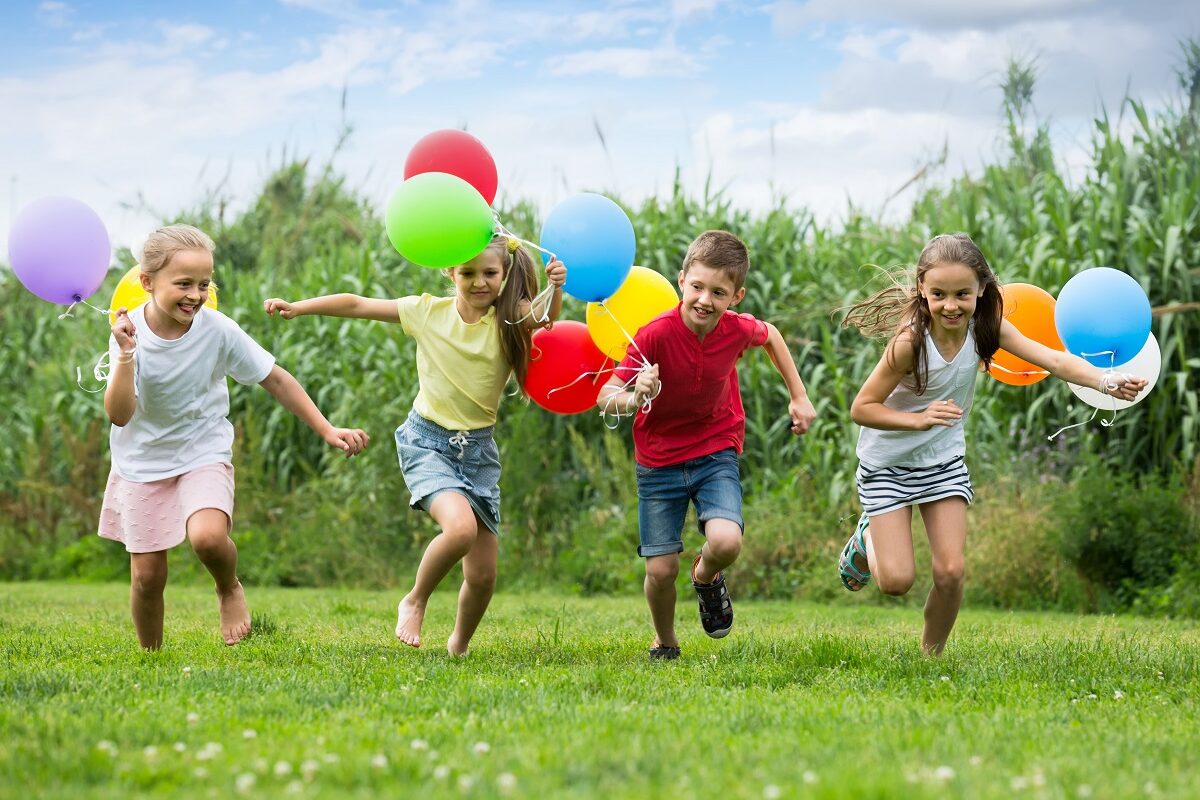 O gașcă de copii în timp ce aleargă pe iarbă și sărbătorește ziua copilului cu baloane colorate