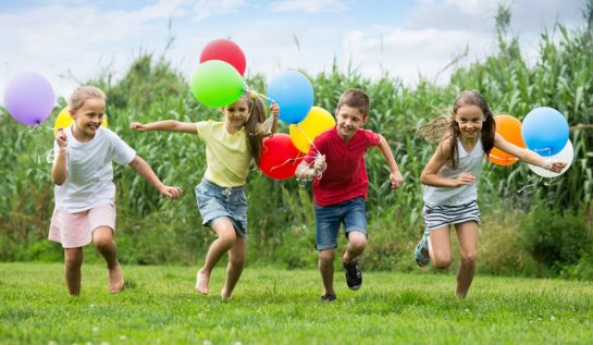 O gașcă de copii în timp ce aleargă pe iarbă și sărbătorește ziua copilului cu baloane colorate