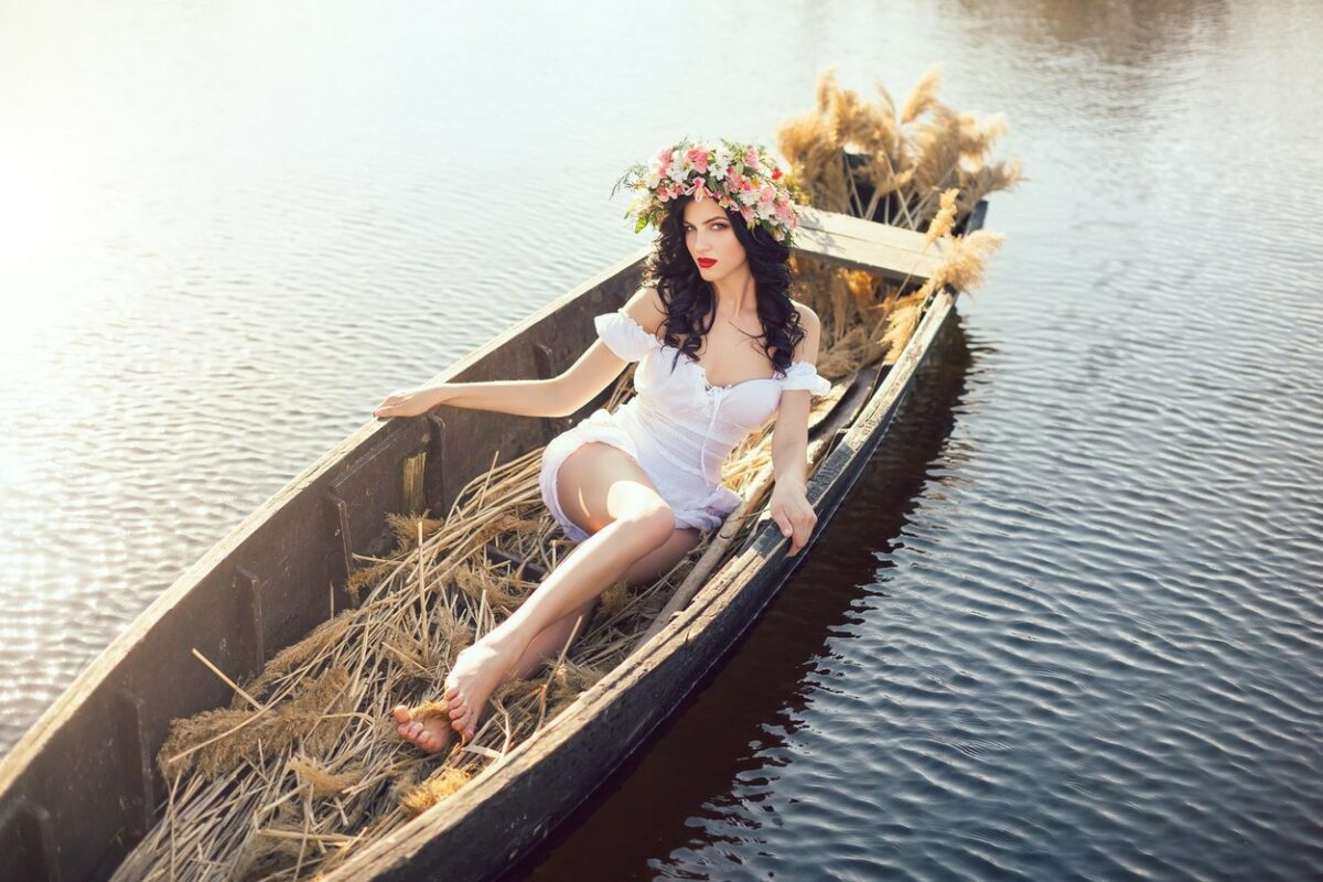 Fată frumoasă îmbrăcată într-o rochie albă scurtă stă într-o barcă plină de paie