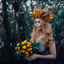 Fată frumoasă în pădure cu o coroniță de flori și cu un buchet de flori în mână