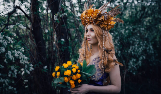 Fată frumoasă în pădure cu o coroniță de flori și cu un buchet de flori în mână