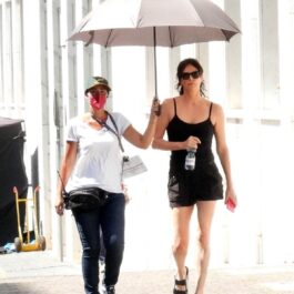 Charlize Theron care s-a vopsit brunetă în timp ce merge însoțită de o femeie care îi ține deschisă o umbrelă de soare