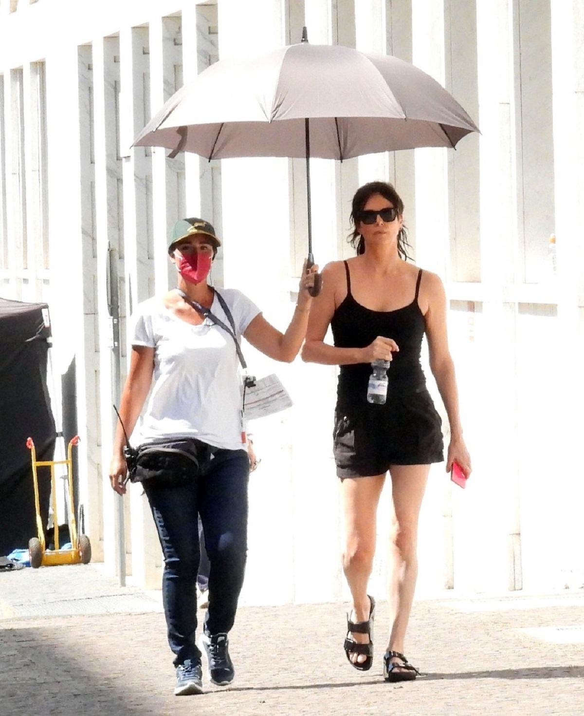 Charlize Theron care s-a vopsit brunetă în timp ce merge însoțită de o femeie care îi ține deschisă o umbrelă de soare