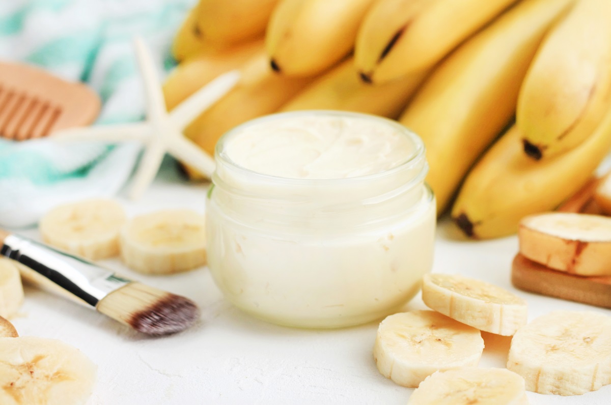 O masă albă pe care se află mai multe banane coapte și un bol mic alb cu mască de păr pentru a ilustra care sunt beneficiile bananelor asupra sănătății părului