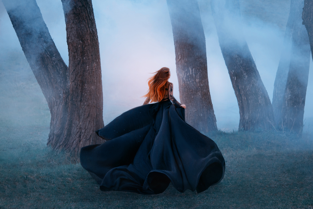 Fată frumoasă îmbrăcată într-o rochie lungă, neagră, aleargă prin pădure