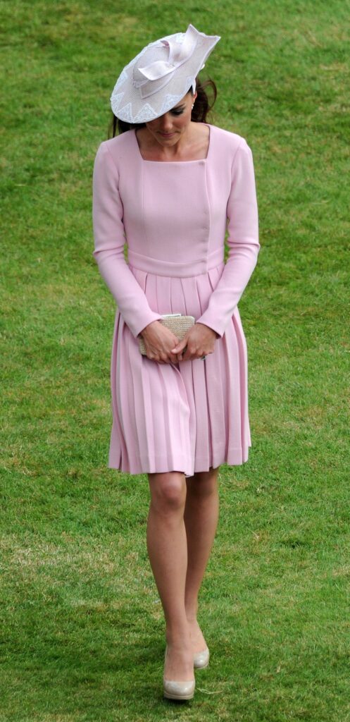 Kate Middleton într-o ținută roz cu o pălărie roz în timp ce ia parte la petrecerea ținută în grădinile palatului Buckingham din anul 2012