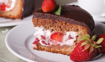 Porție de tort cu mousse de căpșuni și glazură de ciocolată pe o farfurie albă